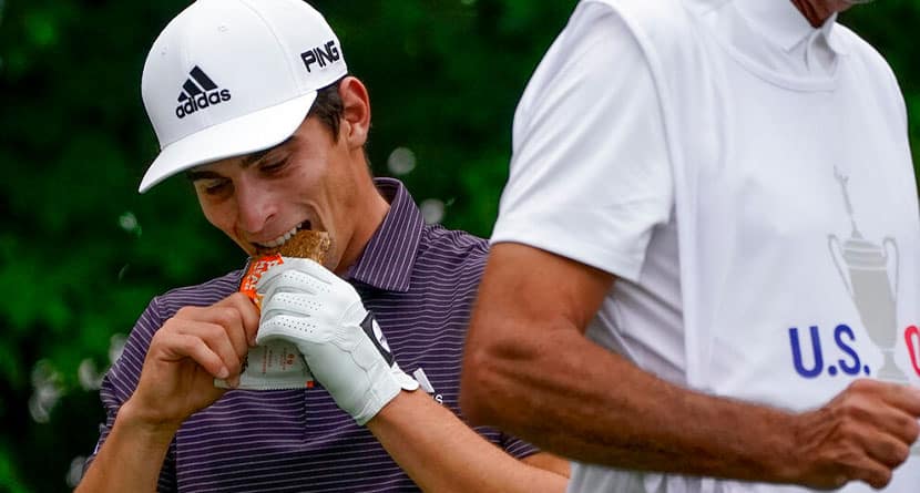 Joaquin Niemann, of Chile, takes a bite of a snack before playing his shot from the 12th tee during the first round of the US Open Golf Championship, Thursday, Sept. 17, 2020, in Mamaroneck, N.Y. (AP Photo/Charles Krupa)