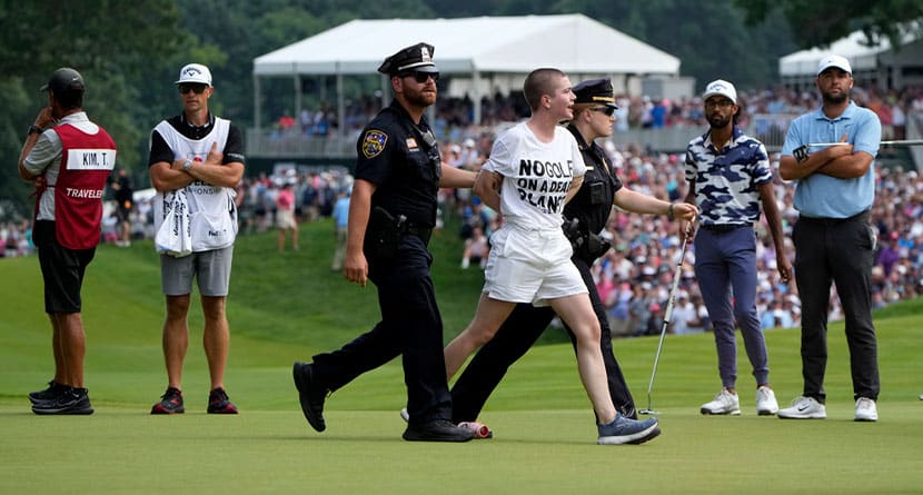 One of several protesters is led away after they ran onto the course on at the 18th hole as Akshay Bhatia, second from right, and Scottie Scheffler, right, watch during the final round of the Travelers Championship golf tournament at TPC River Highlands, Sunday, June 23, 2024, in Cromwell, Conn. (AP Photo/Seth Wenig)