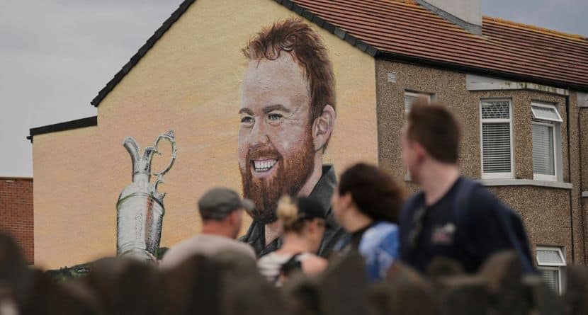 A woman walks past a mural of golfer Shane Lowry of Ireland, holding the Claret Jug trophy, in Portrush, ahead of the 2025 British Open golf championship at the Royal Portrush Golf Club, Northern Ireland, Monday, July 14, 2025. (AP Photo/Francisco Seco)